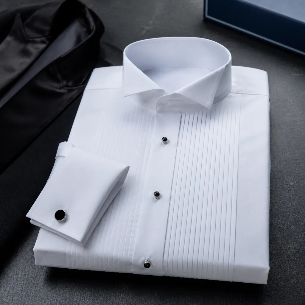 Formal tuxedo shirt with pleated front and cufflinks laid flat on a dark surface